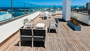 Une terrasse sur le toit avec une plateforme en bois, des meubles d’extérieur blancs et une vue sur l’océan.