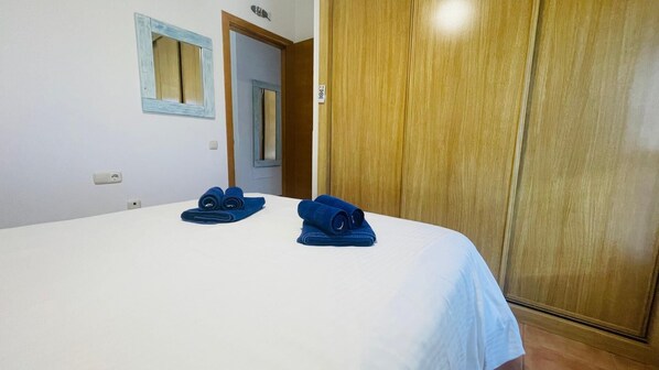 A neatly made bed with blue towels, a wooden wardrobe, and a small mirror on the wall.