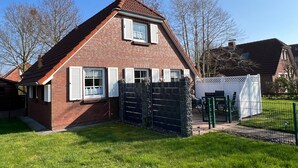 Une maison à deux étages, construite en briques, avec un toit en pente, des volets blancs et une cour arrière clôturée.