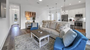 A spacious living room with a sofa, coffee table, and a view of the kitchen.