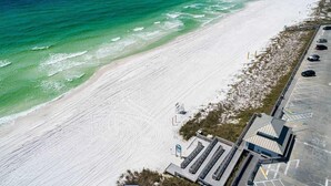 An aerial view of a beach with a parking area and a building with a sloped roof.