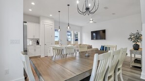 A modern kitchen with white cabinets, a wooden dining table, and pendant lights.