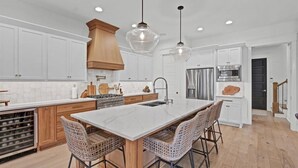 Una cocina moderna con armarios blancos, una isla grande con taburetes de bar, electrodomésticos de acero inoxidable e iluminación colgante.