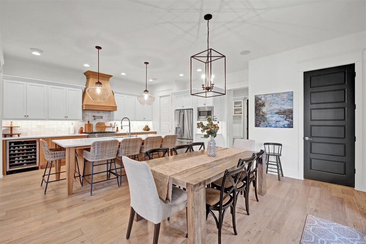 A modern kitchen with white cabinets, a wooden dining table, and a black door.