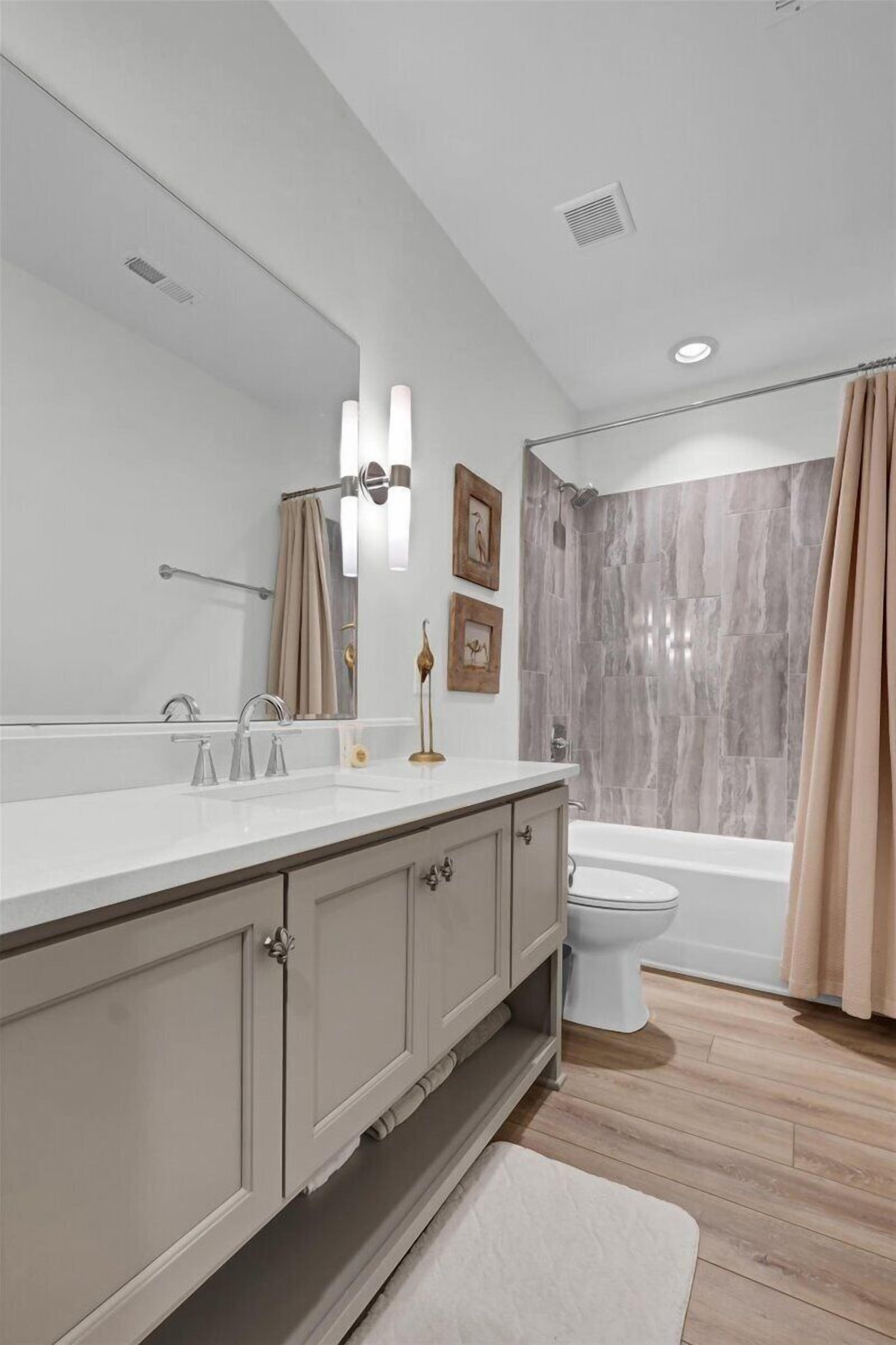 A modern bathroom with a large mirror, dual sinks, a toilet, and a shower area.