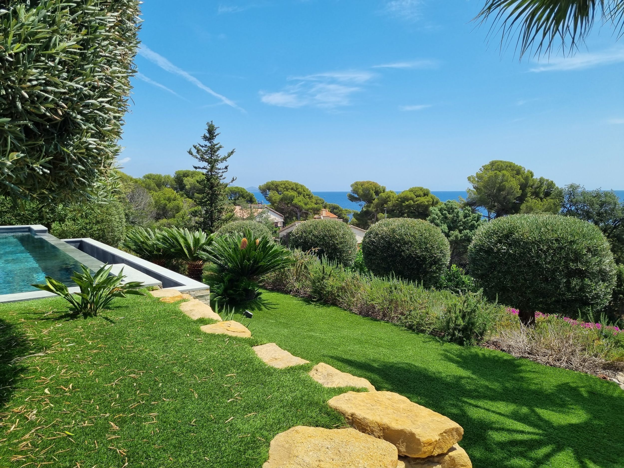 Ein gepflegter Garten mit Schwimmbad, Steintreppe und Meerblick.