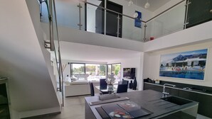 A modern kitchen with a central island, a dining area with a glass table, and a view of a pool and outdoor seating. - Cap malouins  - Four Bedroom Villa, Sleeps 8 (Roquebrune-sur-Argens)