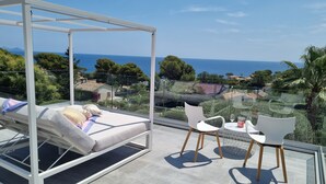 A balcony with a bed, two white chairs, and a table with a wine glass and candle. - Cap malouins  - Four Bedroom Villa, Sleeps 8 (Roquebrune-sur-Argens)