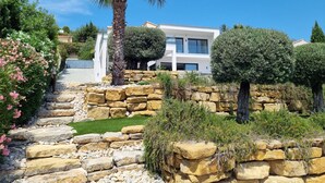 A modern house with a stone pathway leading to the entrance, surrounded by well-maintained gardens and a clear blue sky. - Cap malouins  - Four Bedroom Villa, Sleeps 8 (Roquebrune-sur-Argens)