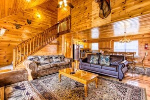 Cozy living area with a high ceiling, featuring a sofa set, armchair, and wooden coffee table.