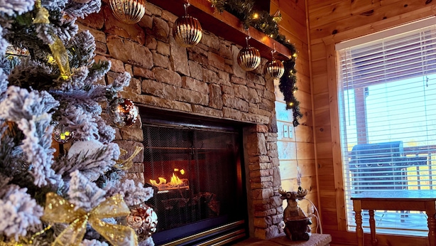 Una chimenea acogedora con repisa de piedra, un árbol de Navidad decorado y un interior rústico de madera.