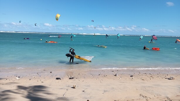 Una playa con cielos despejados y gente practicando deportes acuáticos.
