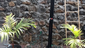 Un muro de piedra con una fuente negra, rodeado de plantas en macetas y una escalera.