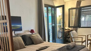 Habitación de hotel con cama, escritorio, silla, espejo y vistas al exterior.