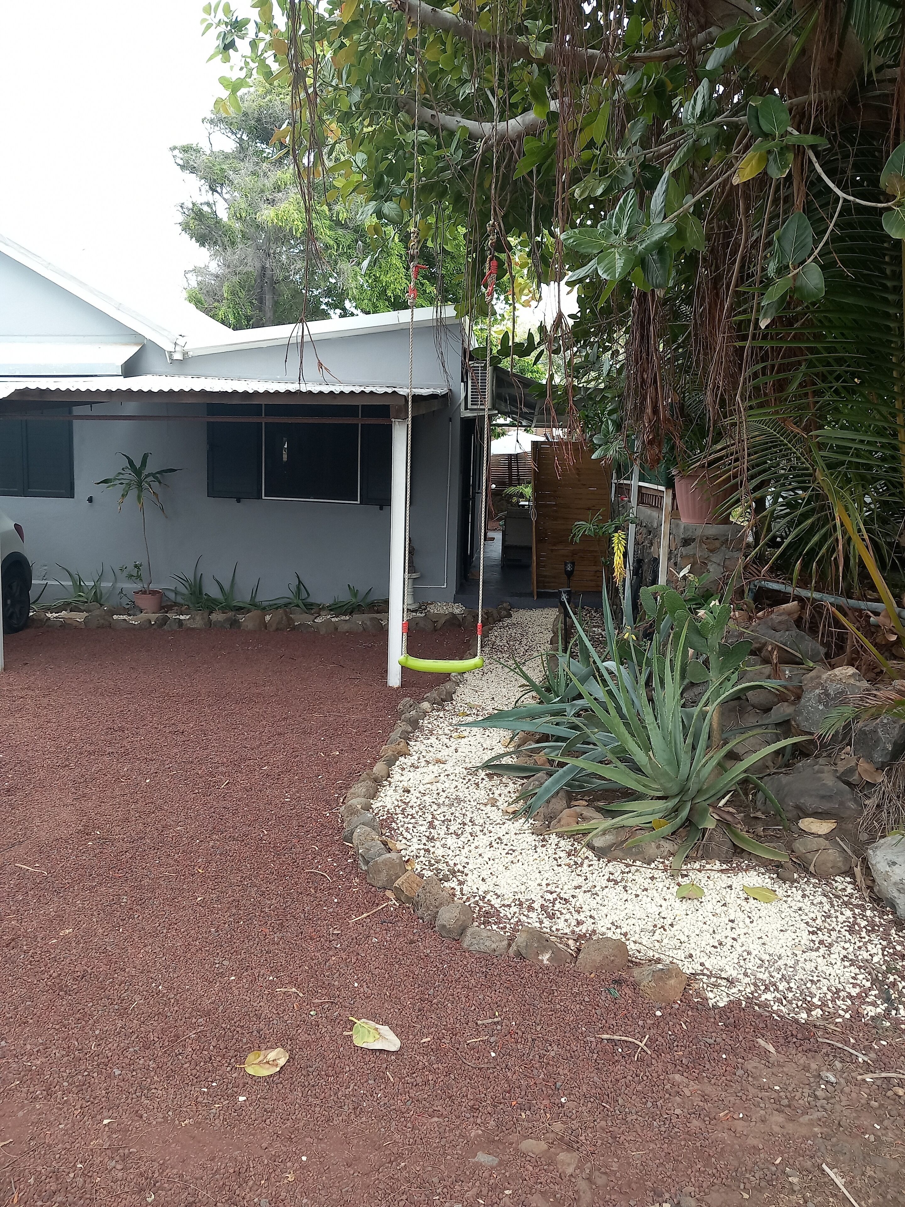 Una casa con un portico coperto, un'altalena e un giardino con diverse piante e un vialetto in ghiaia.