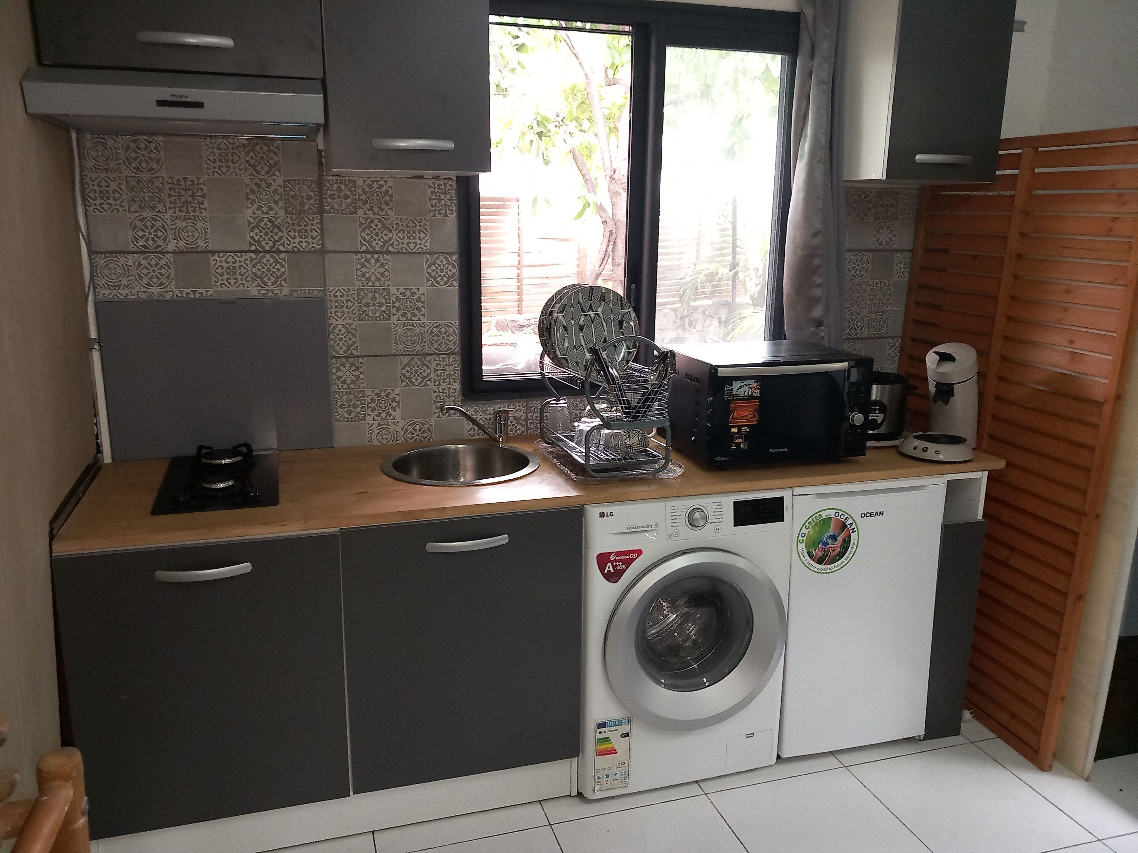 Eine kompakte Küche mit Waschmaschine, Spüle, Fenster und Mikrowelle.