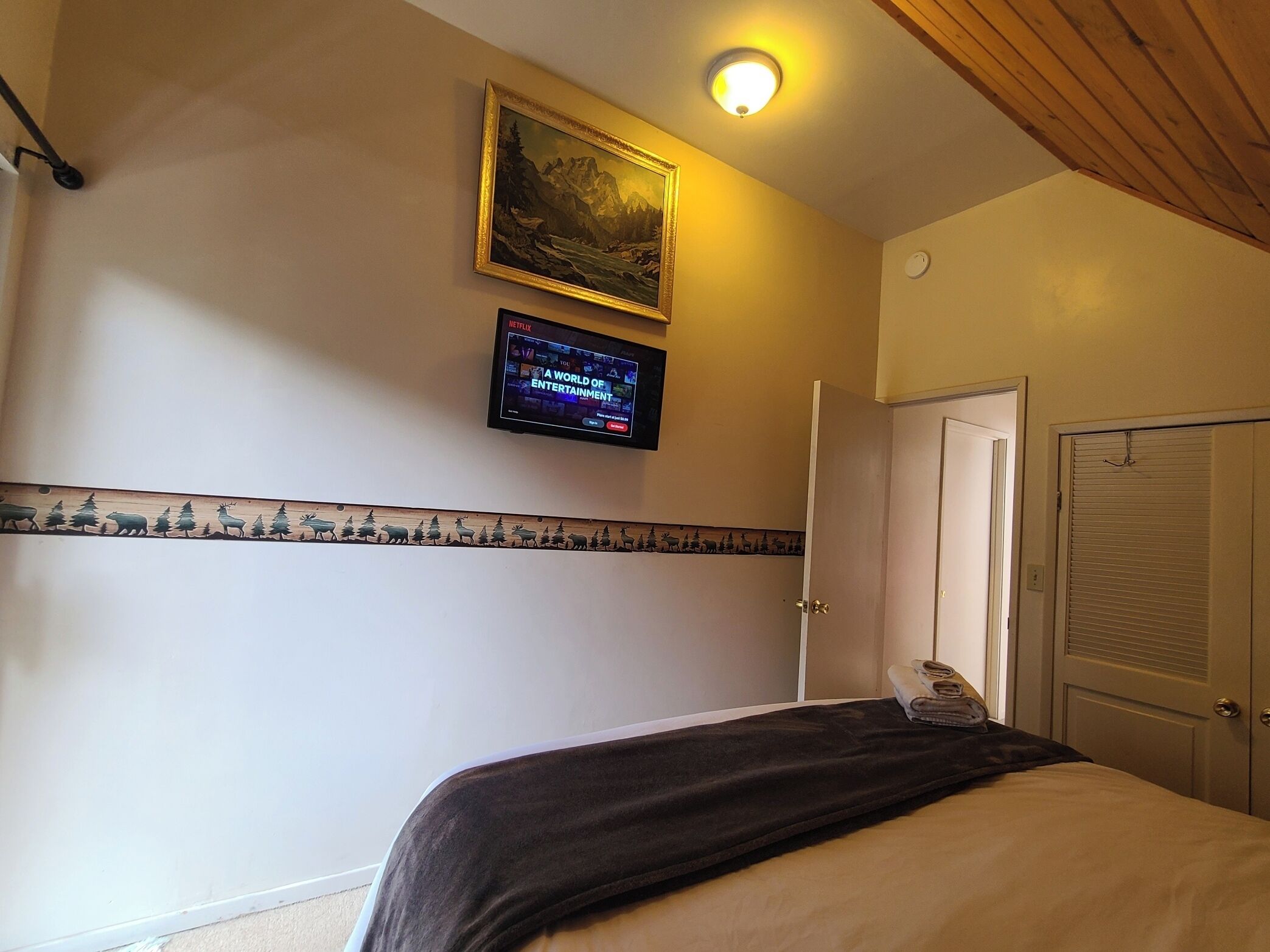 A bedroom with a bed, a television mounted on the wall, a door, and a ceiling light.