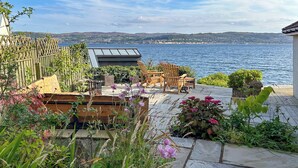 A patio with outdoor furniture, a view of the sea, and a garden with various plants. - 2 bedroom accommodation in Kilcreggan, near Helensburgh (Kilcreggan, near Helensburgh)