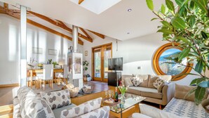 A modern living room with a sofa, coffee table, and a TV. There is a dining area with chairs and a table, and a kitchen area with a stove. - 2 bedroom accommodation in Kilcreggan, near Helensburgh (Kilcreggan, near Helensburgh)