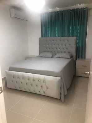 Une chambre à coucher avec un grand lit, une table de chevet, un tiroir et un climatiseur fixé au mur.