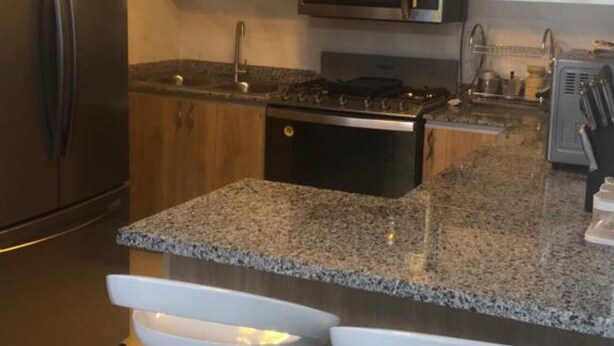 Une cuisine moderne dotée de plans de travail en granit, d’appareils électroménagers en acier inoxydable et de luminaires suspendus.