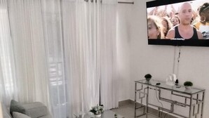 Un salon avec un canapé gris, une table basse en verre et un téléviseur fixé au mur.