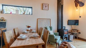A cozy dining area with a wooden table set for four, surrounded by leather chairs. A rustic wall clock and a framed map are visible. - Outshot Barn - sleeps 4 guests in 2 bedrooms, Hay-on-Wye (Hay-on-Wye)