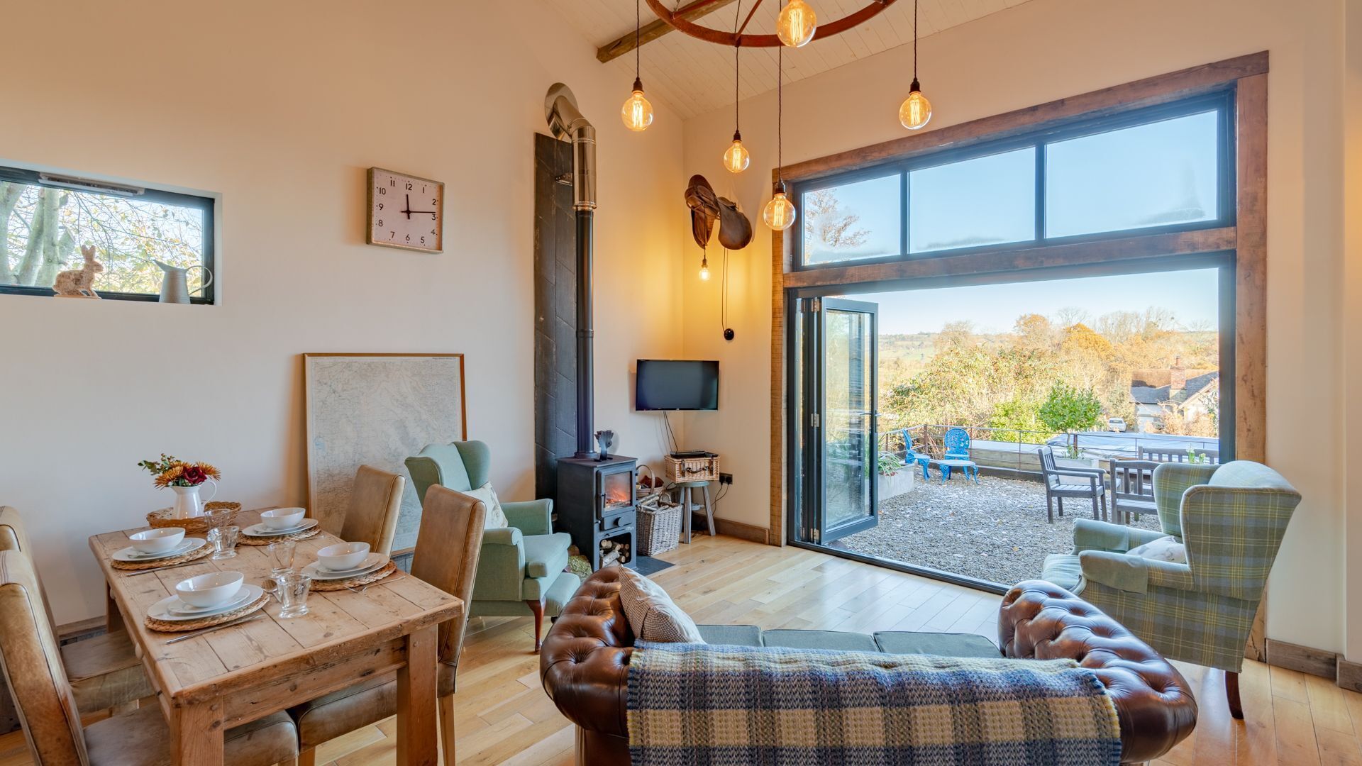 Un salon chaleureux avec une cheminée, un coin repas avec des meubles en bois et une grande fenêtre donnant sur l’extérieur.