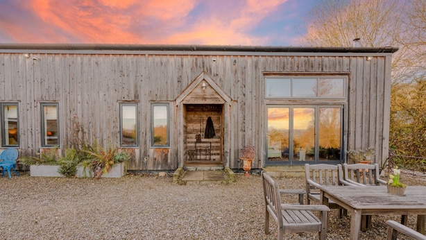A rustic wooden building with a large window, a door, and a gravel driveway. - Outshot Barn - sleeps 4 guests in 2 bedrooms, Hay-on-Wye (Hay-on-Wye)