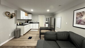 A modern kitchen with white cabinets, a stainless steel refrigerator, and a dining area with a black table and grey sofa. - Madison’s Place UNIT B (Peoria)