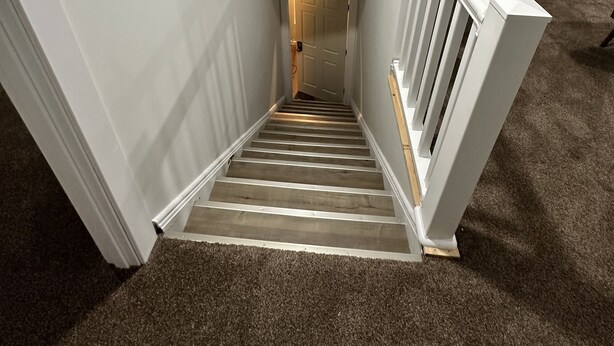 A narrow staircase with a wooden handrail and carpeted steps leading to a door at the top. - Madison’s Place UNIT B (Peoria)