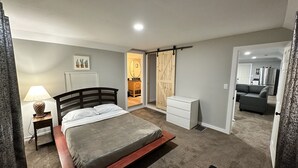 A bedroom with a bed, bedside table, lamp, and a sliding door leading to a bathroom. - Madison’s Place UNIT B (Peoria)