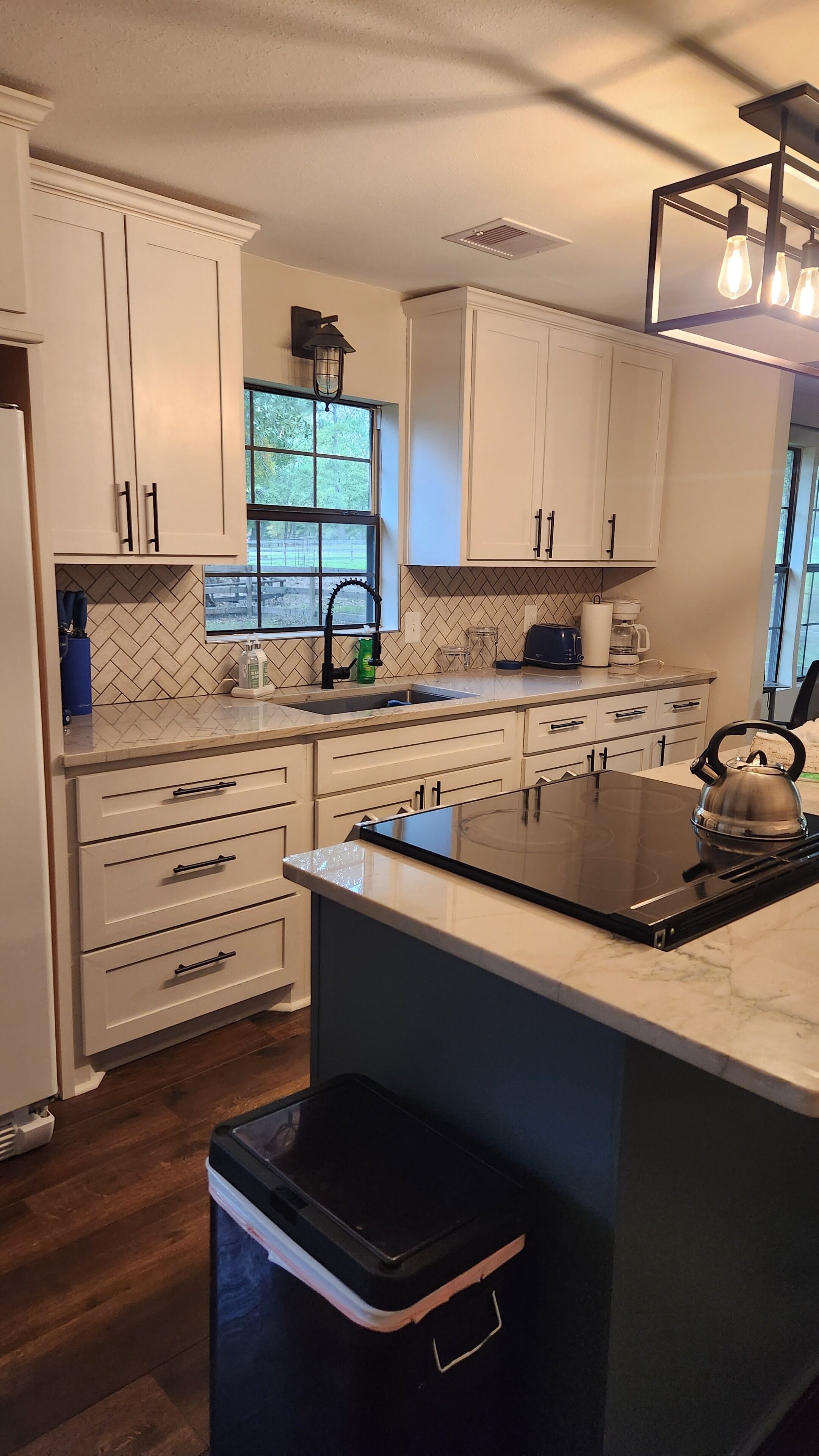 A modern kitchen with white cabinets, a black countertop, and a stainless steel kettle.