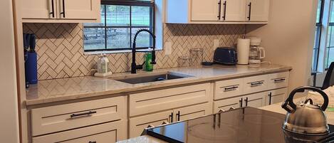 A modern kitchen with white cabinets, a black countertop, and a stainless steel kettle.