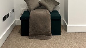 Habitación de esquina con un sofá verde, dos almohadas, una manta marrón y una cesta redonda de mimbre con adornos en la pared.