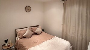Un dormitorio con cama, mesita de noche, reloj y ventana con cortinas.