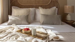 Cama bem arrumada com bandeja de morangos e leite, abajur e cabeceira de vime.