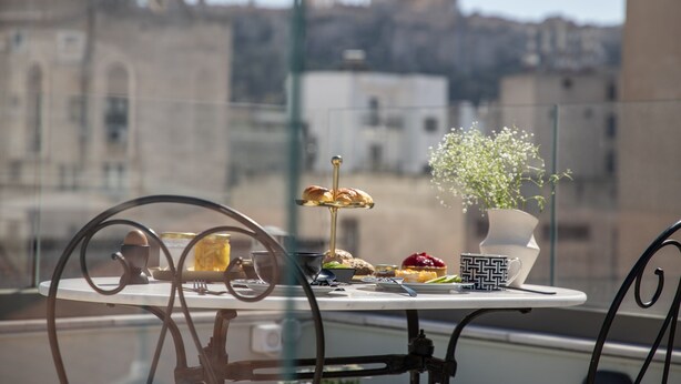 Uma mesa com diversos alimentos e um vaso de planta numa varanda com vista para a cidade.