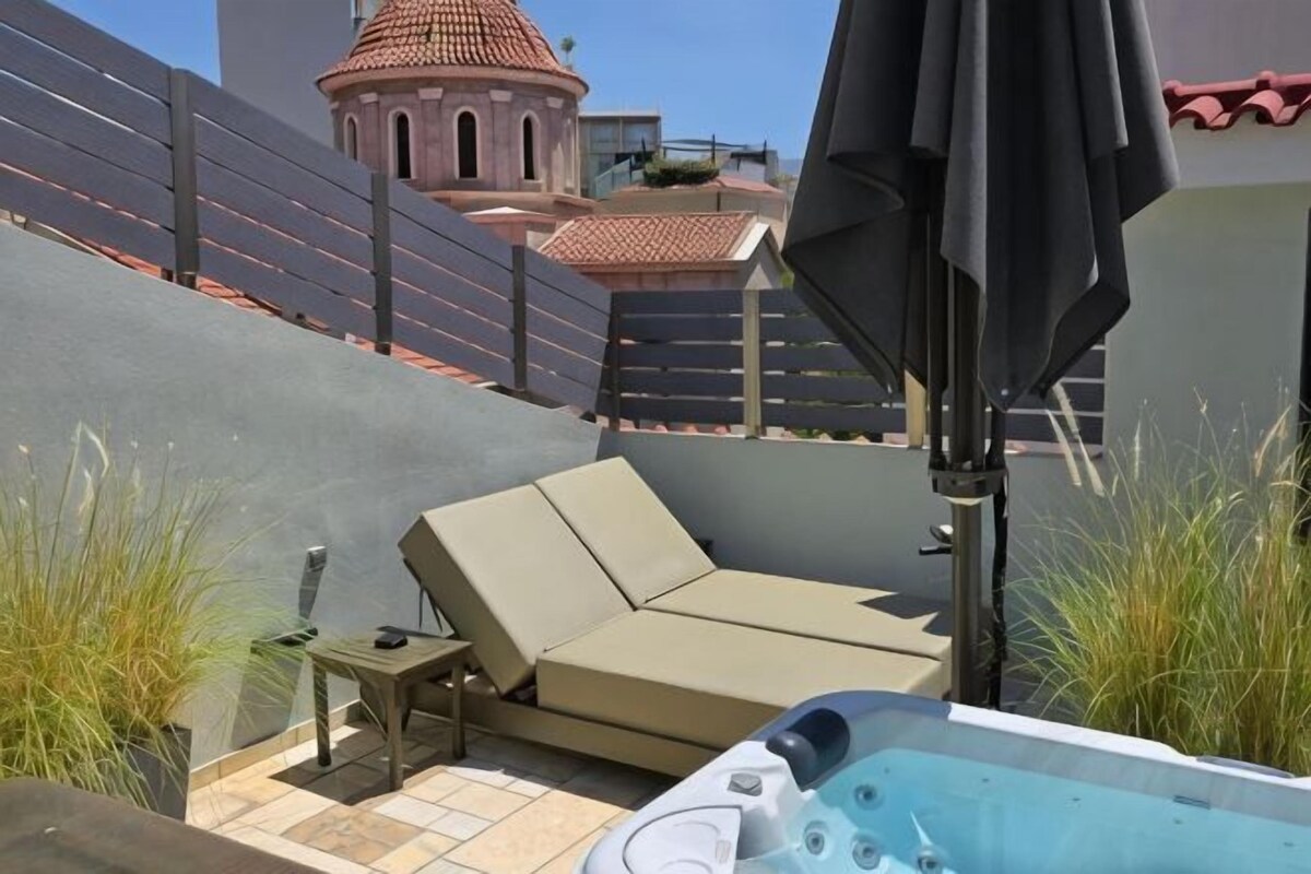 Una terraza en la azotea con un jacuzzi, un sofá color beige y una mesita.