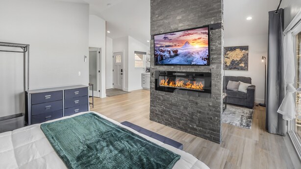 A modern bedroom with a large bed, a fireplace, a mounted TV, and a view of the living area. - Mountain Escape With Fireplace (Show Low)