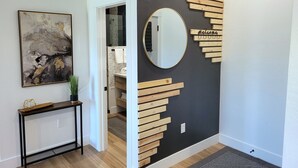 A hallway with a modern art piece, a console table, a mirror, and a wooden wall decoration with a 'Welcome' sign. - Mountain Escape With Fireplace (Show Low)