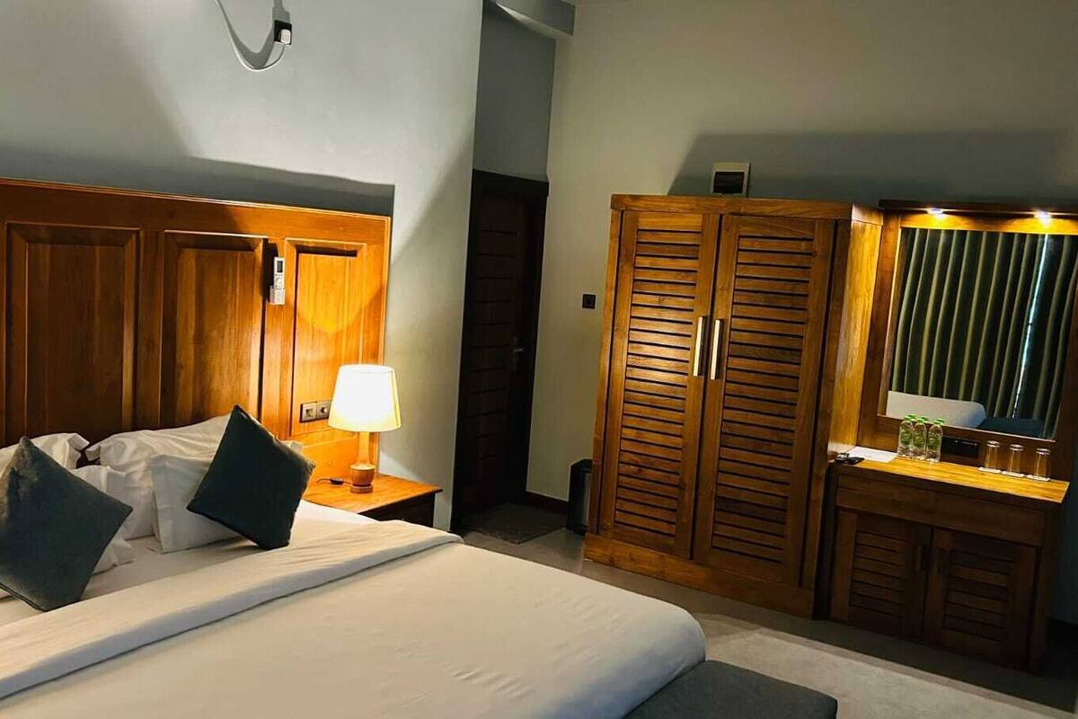 Une chambre d’hôtel comprenant un lit, une table de chevet, une lampe, une armoire en bois et un miroir.