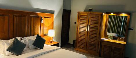 Una habitación de hotel con cama, mesita de noche, lámpara, armario de madera y espejo.