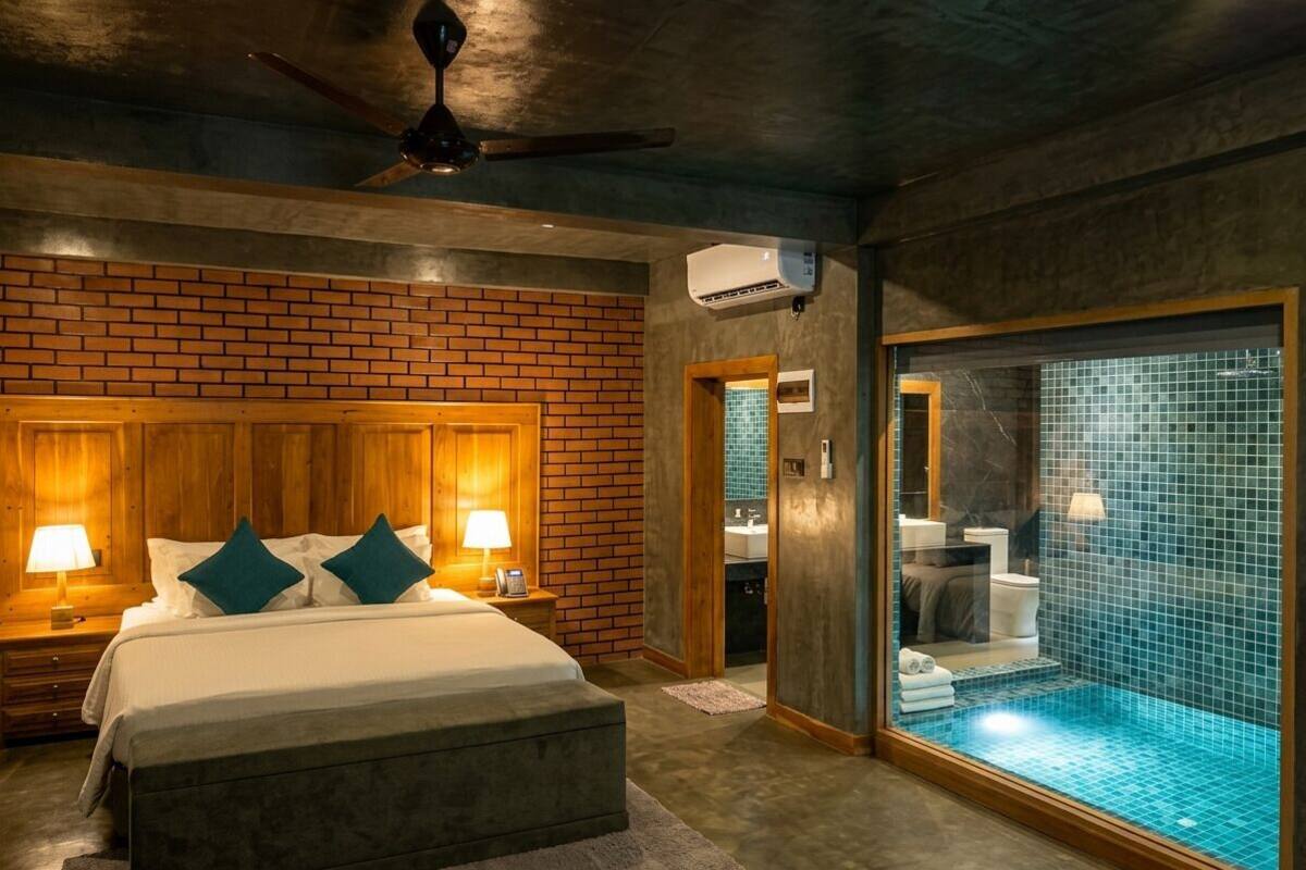 Une chambre avec un mur en briques, un lit avec des oreillers, une table de chevet, un ventilateur de plafond et un appareil de climatisation.
