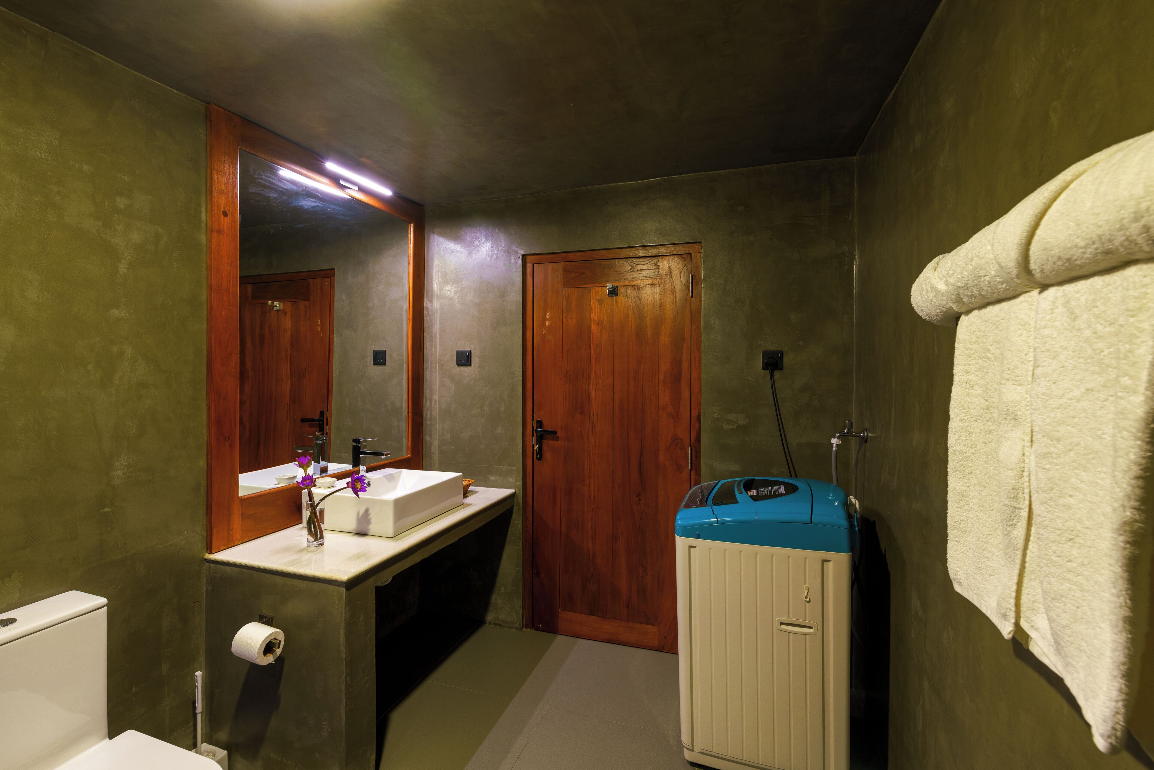 A bathroom with a wooden door, a sink, a toilet, and a blue washing machine.