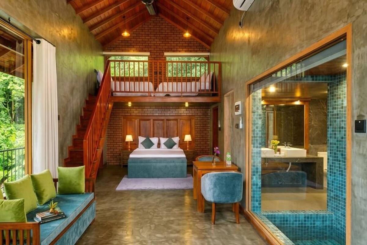 Une pièce spacieuse avec un plafond en bois, un balcon, une grande fenêtre, un lit, un coin salon et une salle de bain avec un mur carrelé.