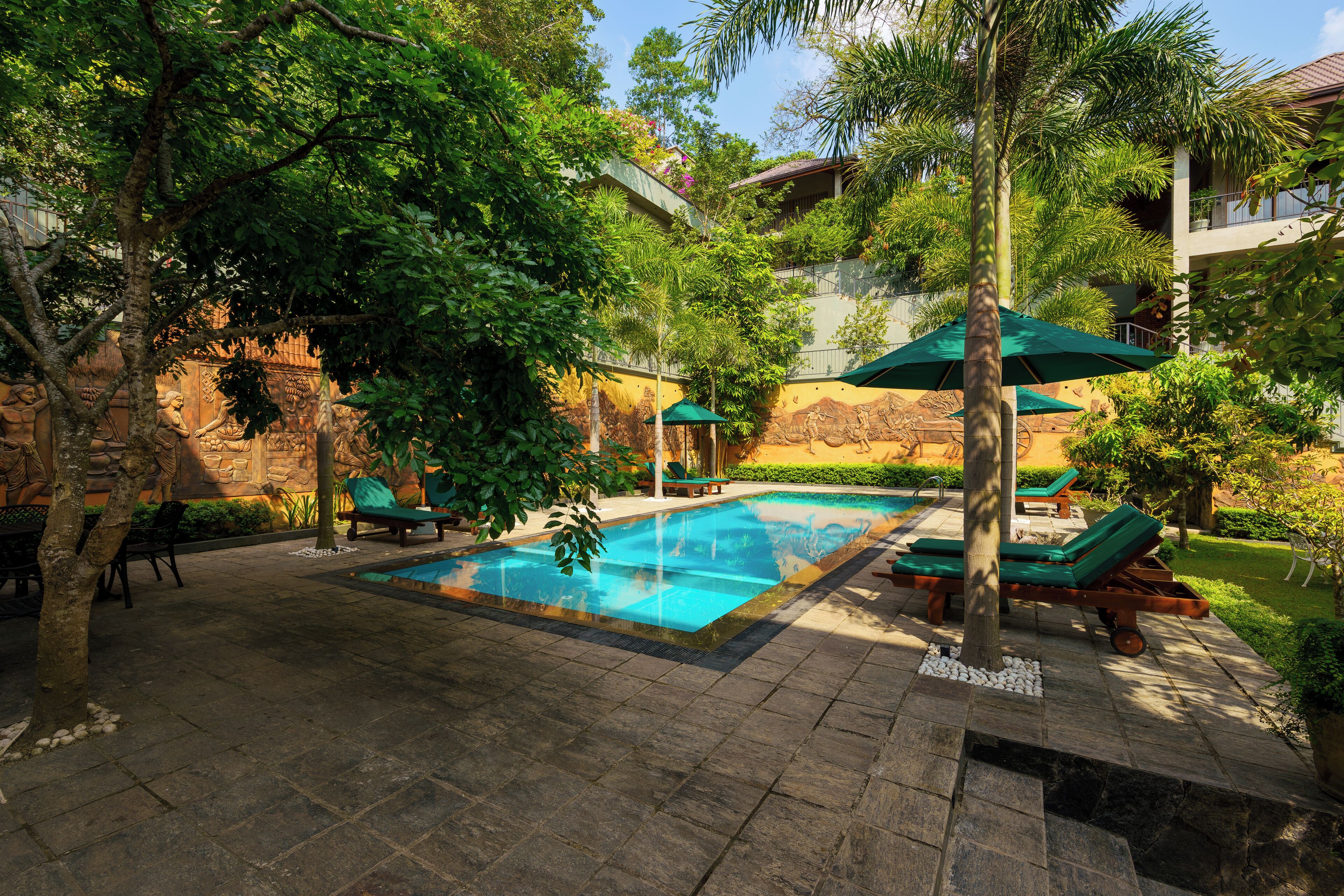 A pool area with lounge chairs and umbrellas, surrounded by greenery and stone walls.