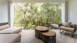 A modern outdoor living area with a sofa, a round wooden table, and a view of a lush garden. - ANANA Yaaxlum 105 S (Tulum)