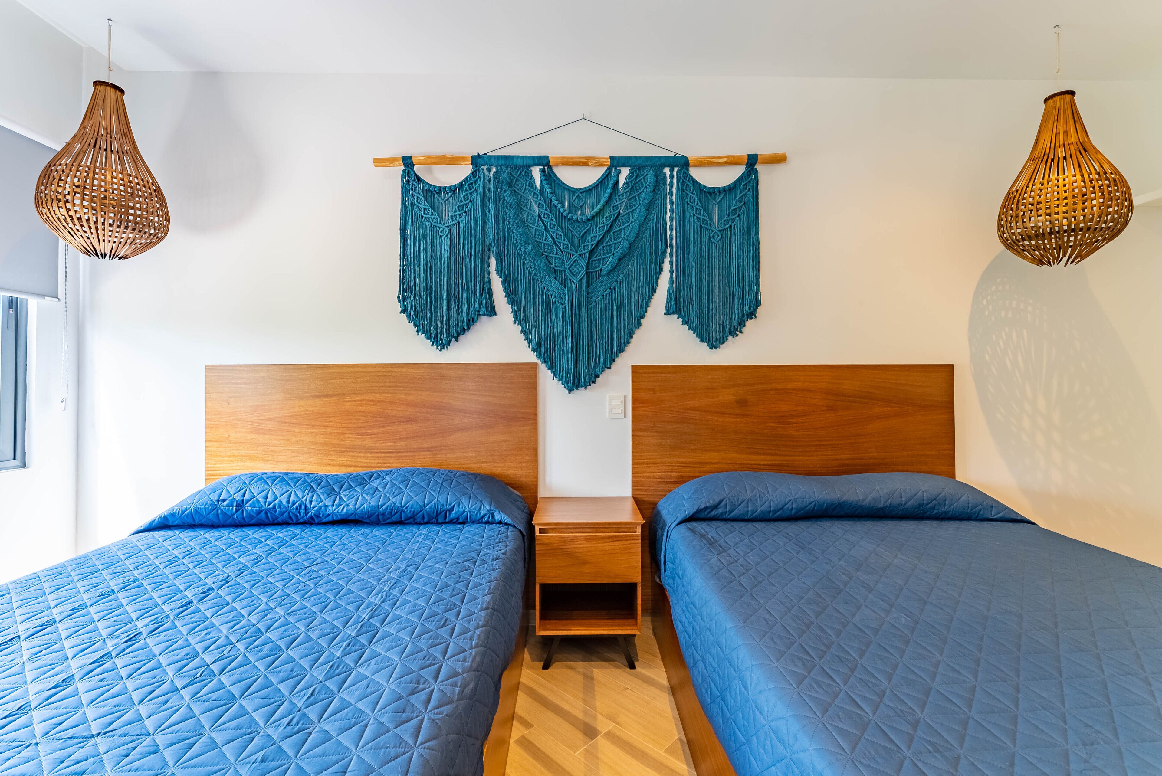 A bedroom with two beds, wooden headboards, a wooden nightstand, and a macrame wall hanging.