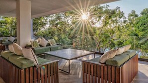 An outdoor seating area with green cushioned sofas and a central coffee table, surrounded by a wooden fence and lush greenery. - ANANA Yaaxlum 105 S (Tulum)